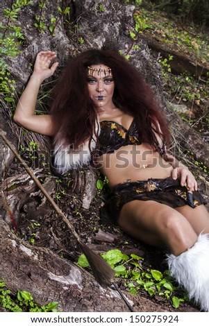 View of a beautiful young strong hunter warrior woman next to a tree.