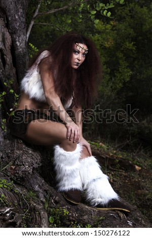 View of a beautiful young strong hunter warrior woman next to a tree.