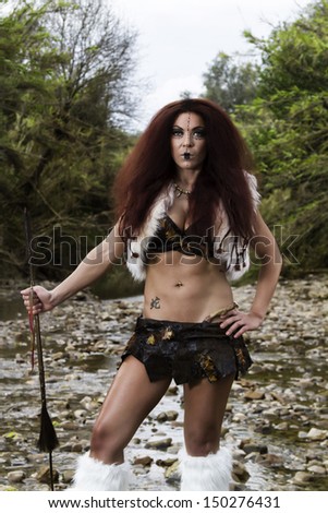 View of a beautiful young strong hunter warrior woman next to a river.