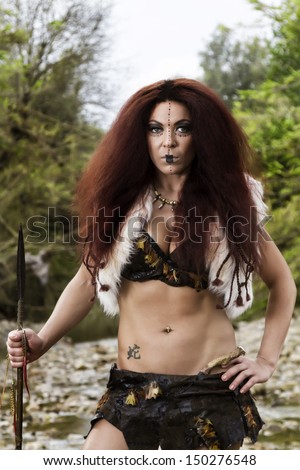 View of a beautiful young strong hunter warrior woman next to a river.