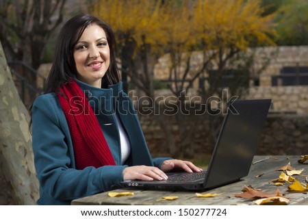View of a beautiful young woman working on a laptop on a urban park.