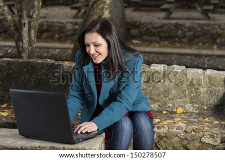 View of a beautiful young woman working on a laptop on a urban park.