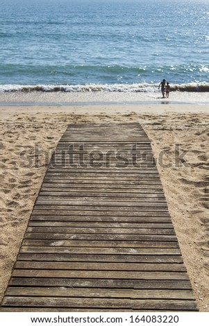 Close up view of a wood board walk in the beach pointing to the sea.