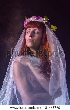 Mysterious and sensual girl with a transparent cloth with a crown of flowers isolated on a black background.
