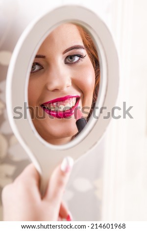 View of a beautiful redhead girl applying lipstick.