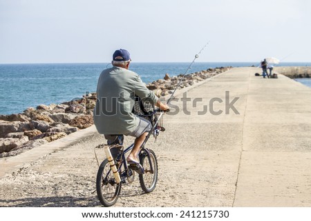 View of a long pier water breaker with a fisherman on a bike moving around.