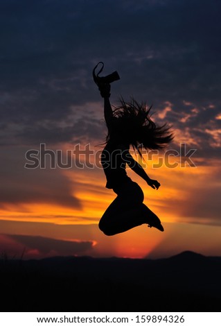 Girl silhouette jumping with photo camera in hand in sunset. Low key shot.