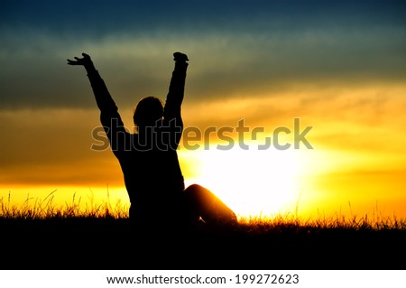 Silhouette of standing woman with rising hands, sunset sky as a