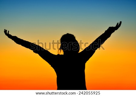Girl silhouette raising hands in sunset light.