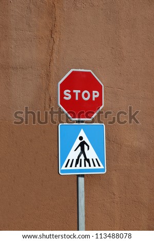 A Stop Sign and Pedestrian Crossing sign with tan coloured wall background