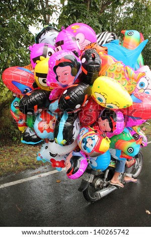 KLUNGKUNG, INDONESIA - JULY 13: A balloon seller on his way to work, has already inflated his balloons before riding his motorbike. July 13, 2012 near Klungkung, Indonesia.