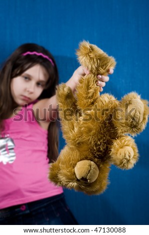 Angry teenage girl holding teddy bear upsidedown