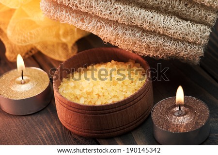 Spa setting with yellow bath salt and lit candles on dark wooden background
