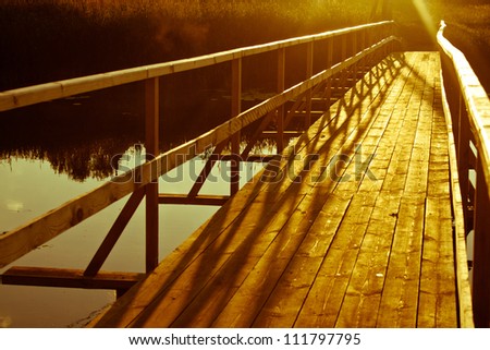 A wooden bridge over the river. Light at the end of the road.
