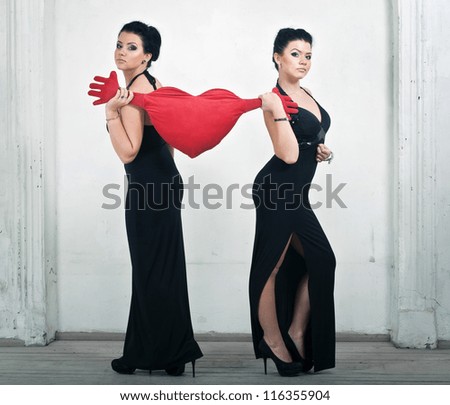 Two elegant women\'s sister pulled a pillow in the shape of heart in different directions.