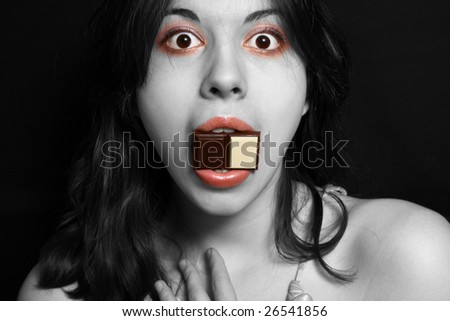 The black-white portrait of the girl scared ly holds a piece of chocolate in a mouth.