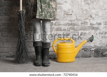 Leg girl in rubber boots and camouflage with a broom and yellow watering can.