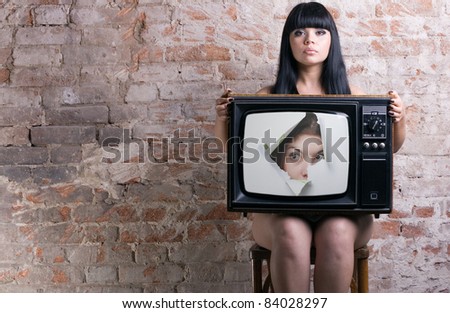 TV with a picture of the girl -facing through a hole in the hands of a seated woman .