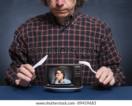 A man with a knife and fork in hand is about to eat with the TV image of the frightened himself.