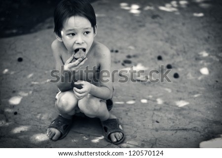 Lone hungry boy eats sitting on the ground.