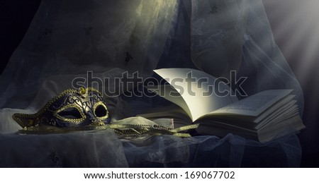 Mystical still life with a carnival mask and an open book.