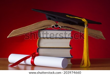 A mortarboard and graduation scroll, tied with red ribbon, on a stack of old battered book