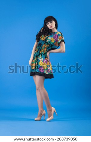 Beautiful young woman in color dress posing on a blue background.
