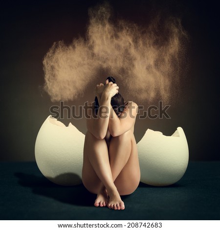 Naked young woman sitting next to a broken egg hiding his hands his head.