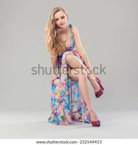 Beautiful young woman sitting in a trendy long dress and shoes.
