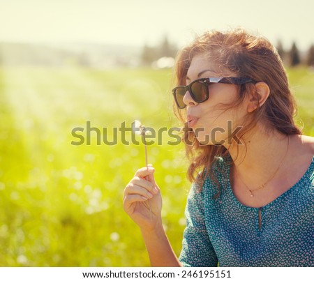 Portrait of a beautiful young woman blowing a dandelion.