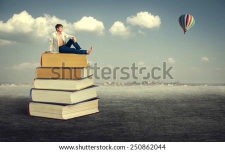 Education. Young man sitting on a pile of books in the open air.