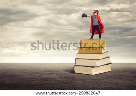 Education. Super hero boy standing on a pile of books in the open air.