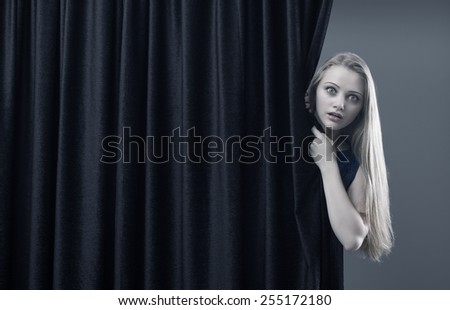 Frightened girl hiding behind a curtain.
