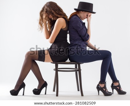 Two offended young women sitting on a chair back to back.