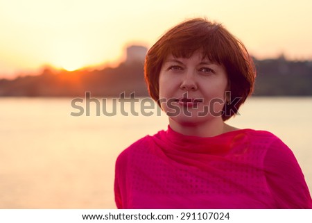 Portrait of a mature woman in the background of the urban landscape with a lake at sunset.