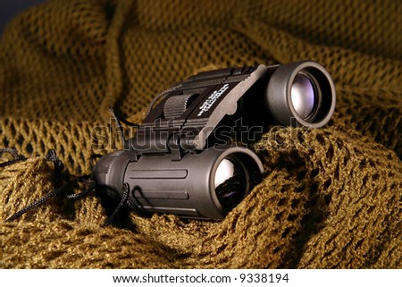 A military black spyglass laid on a camouflage mimetic green scarf