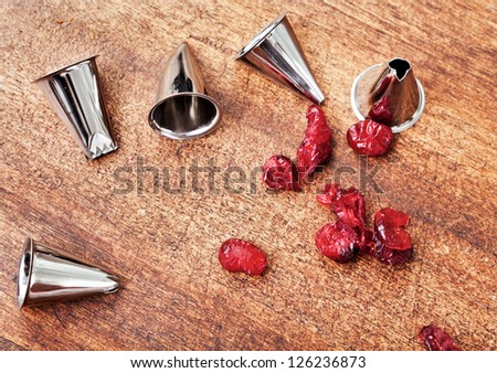 Pastry bag metal tips and red candieds on a wooden table
