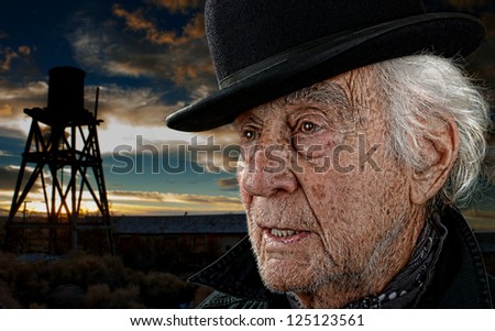 Old man wearing a black bowler hat with an old building and water tower against a dramatic sunset.