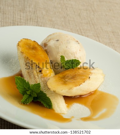 Creamy ice cream on a white plate with bananas topped with brulee in caramel sauce on a white plate with a tan woven placemat