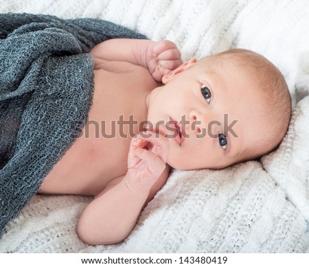 Beautiful wide awake baby lying on a white knit blanket with a soft knit grey blanket on