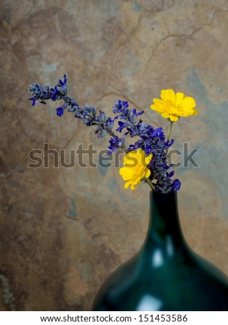 Blue and yellow wildflowers in a turquoise vase against a rustic slate background