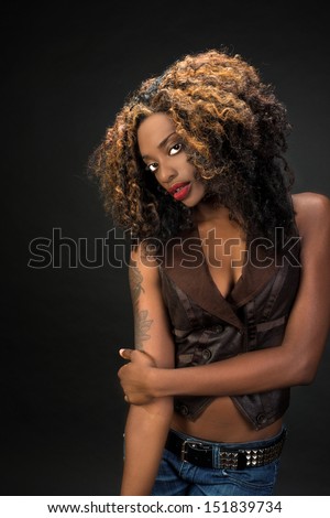 Beautiful African American woman with gorgeous lips wearing jeans and a vest against a dark background