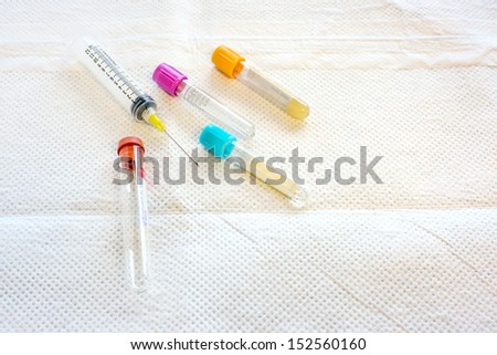 Four test tubes and a syringe for collecting blood on a white disposable pad