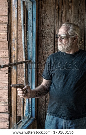 Tough looking old man in an old cabin next to a broken window pointing a vintage pistol
