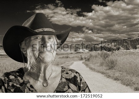 Senior lady wearing a black cowboy hat a rural scene behind her in monochrome