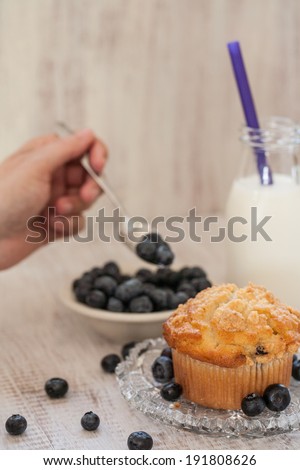Blueberry muffin breakfast with hand spooning blueberries and with glass jug of milk
