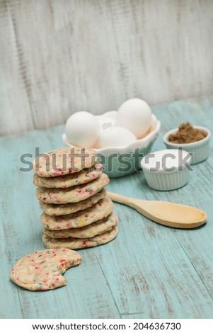Stack of colorful confetti cookies with eggs and sugars and wood spoon