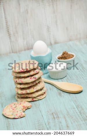 Stack of colorful confetti cookies with egg and sugars and wood spoon