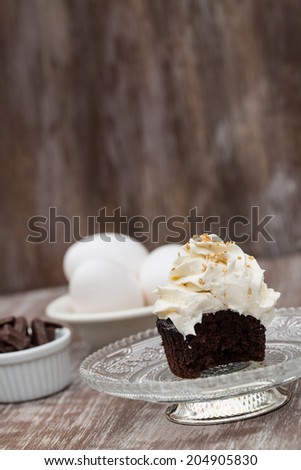 Chocolate cupcake with vanilla frosting missing a bite on antique glass plate with chocolate pieces and eggs