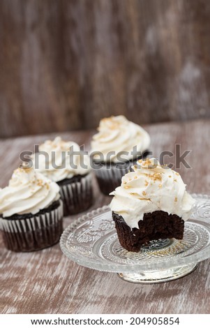 Chocolate cupcakes with vanilla frosting missing a bite on antique glass plate